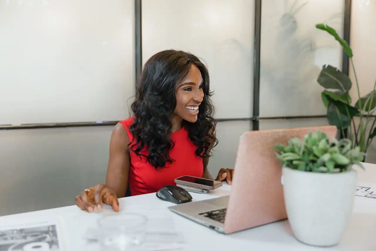 A smiling business owner at her laptop with her phone