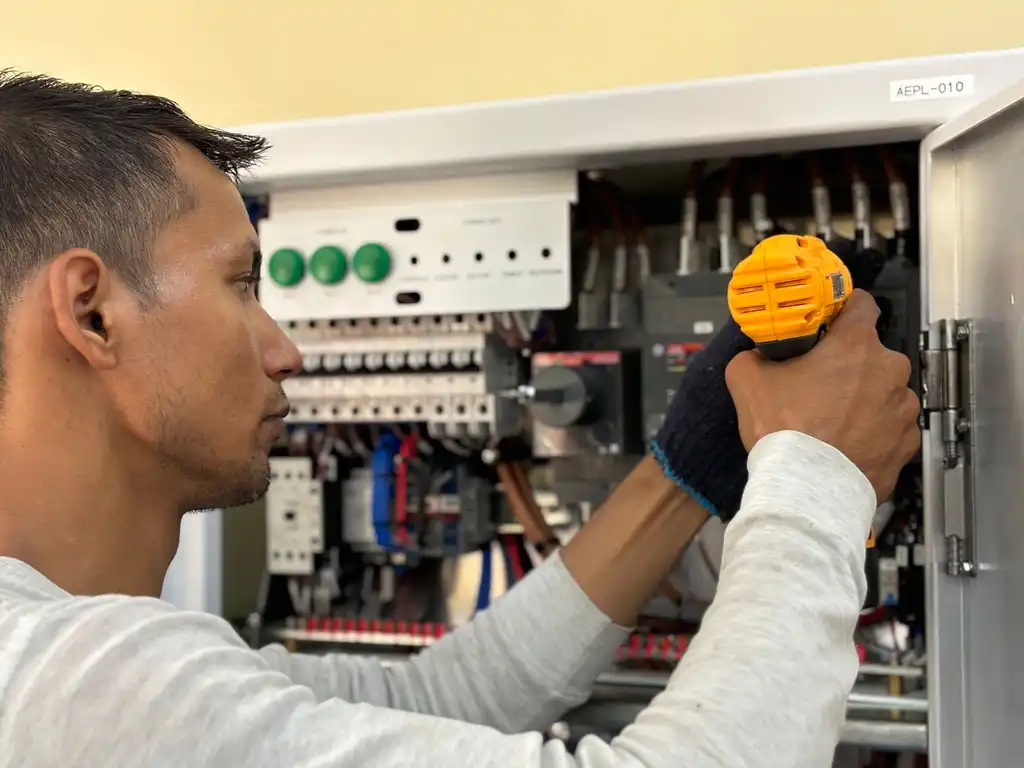 An electrician working on a breaker panel with a drill