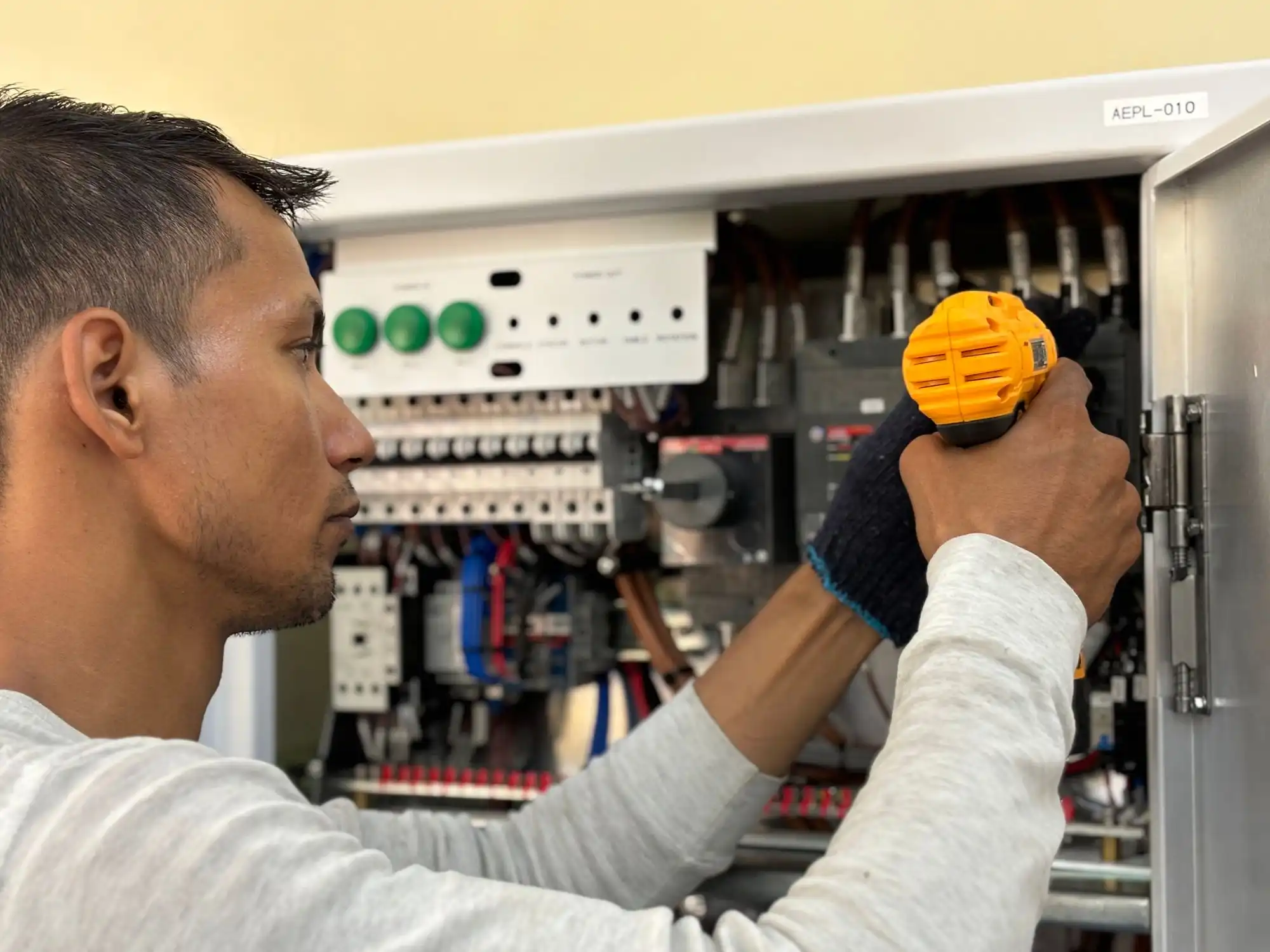 An electrician working on a breaker panel with a drill