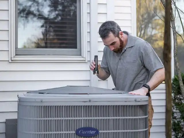 A technician inspecting an outdoor air conditioning unit beside a house