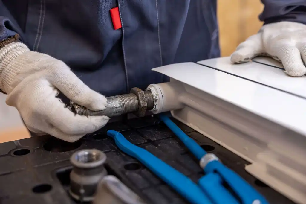 A plumber in gloves fitting a radiator pipe